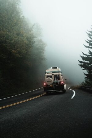 Un van aménagé circulant sur une route de montagne sinueuse et brumeuse en pleine forêt