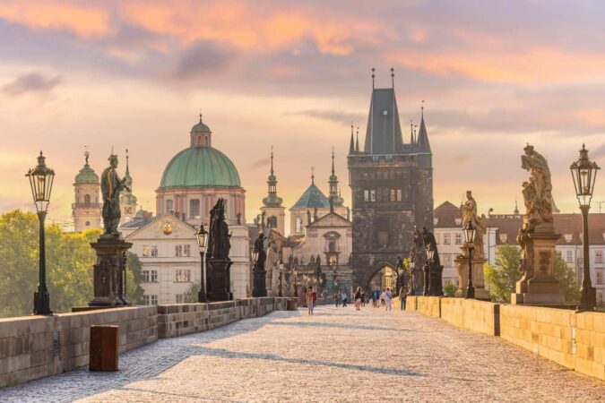 Vue du Pont Charles désert à Prague avec ses statues baroques et la tour du pont de la Vieille Ville sous un ciel de lever de soleil rosé