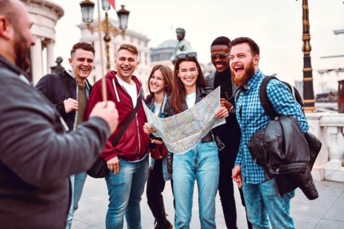 Un groupe de jeunes voyageurs souriants consulte une carte pour choisir le bon tour-opérateur pour leur prochaine aventure.