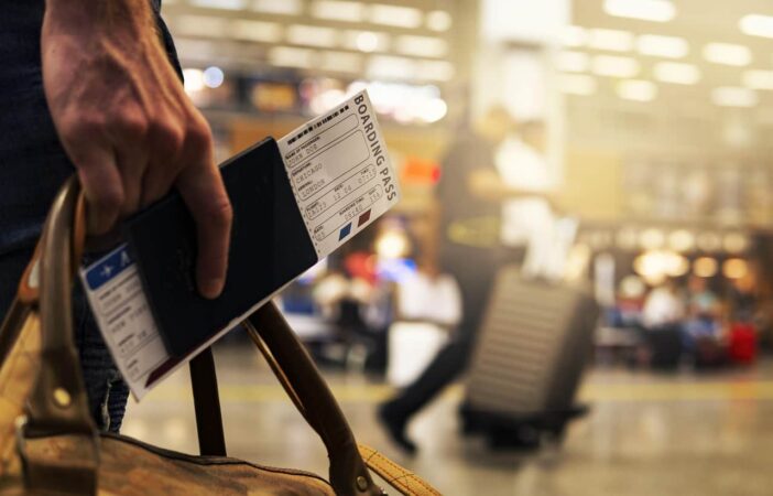 Un voyageur tient un sac en cuir, son billet d'avion pour Londres et les documents requis pour voyager avec son passeport dans un aéroport animé.